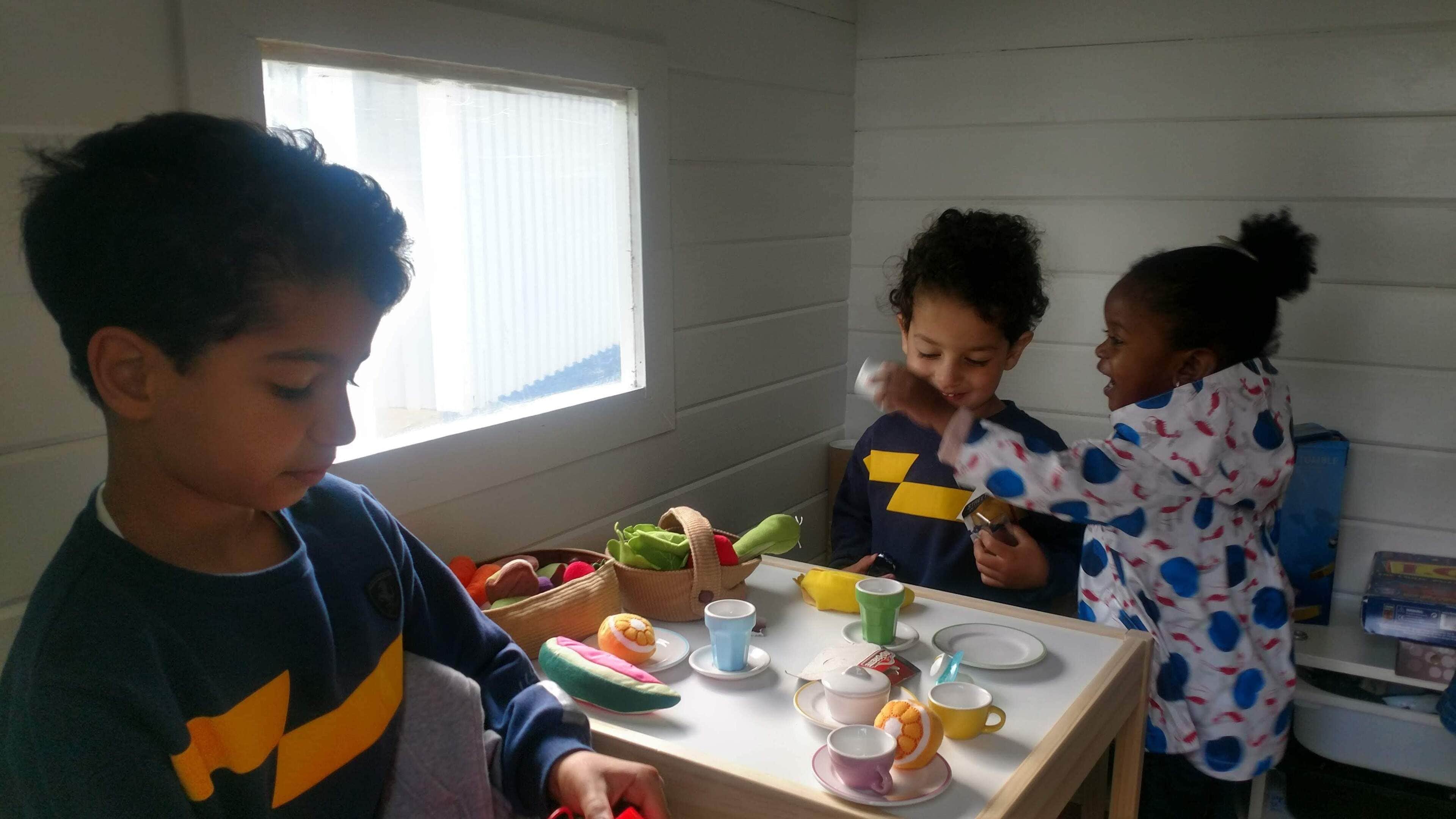Ein Zimmer mit Fenster, Tisch mit Kinderspielzeug und Bechern, und ein Kind in einem blauen Hemd.