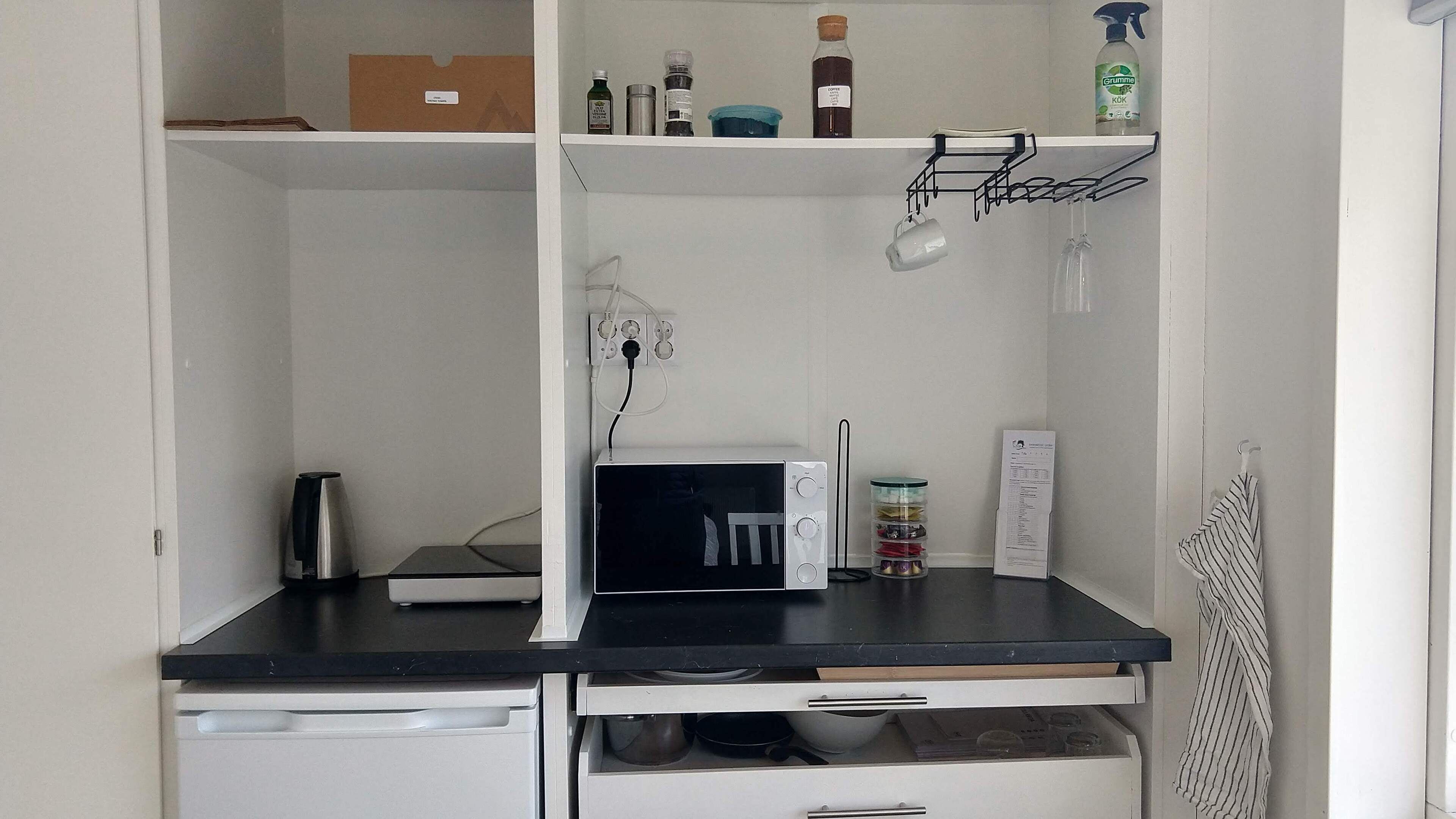 A kitchenette with a microwave, coffee maker, and various kitchen items on shelves.