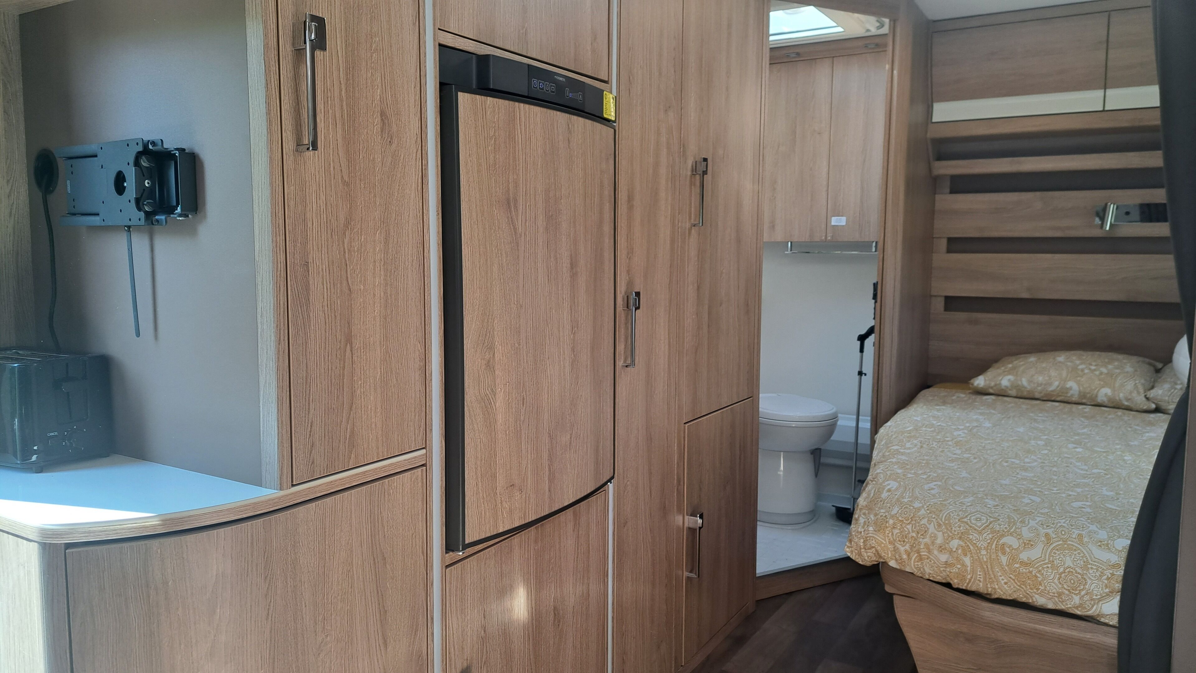 A compact, well-organized room with a bed, a toilet, and a kitchenette area.