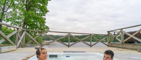 Une terrasse en bois avec un jacuzzi et une vue sur un lac et une forêt.