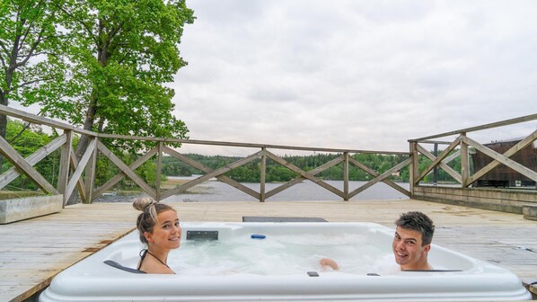 A wooden deck with a hot tub and a view of a lake and forest. - Évika boutique hotel (Landvetter)