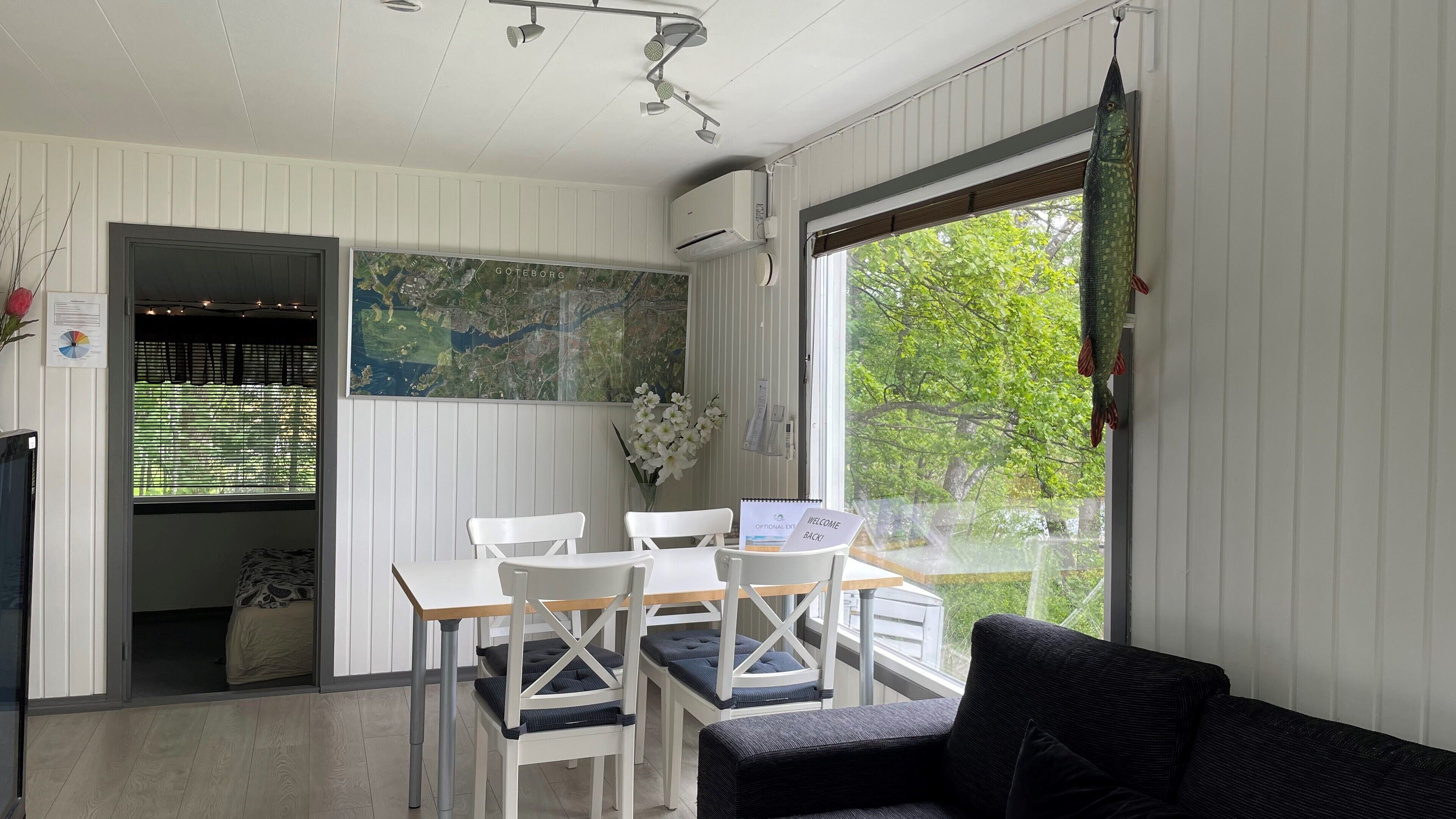 A room with a dining table, chairs, a sofa, a large window with a view of greenery, and a map on the wall.