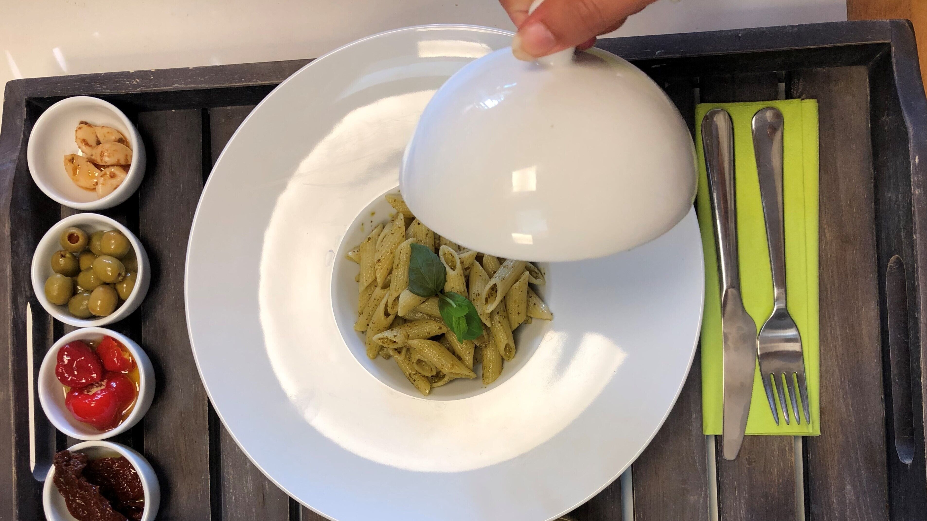 En tallrik pasta med en vit skål ovanpå, serverad tillsammans med små skålar med oliver, körsbärstomater och torkade tomater.