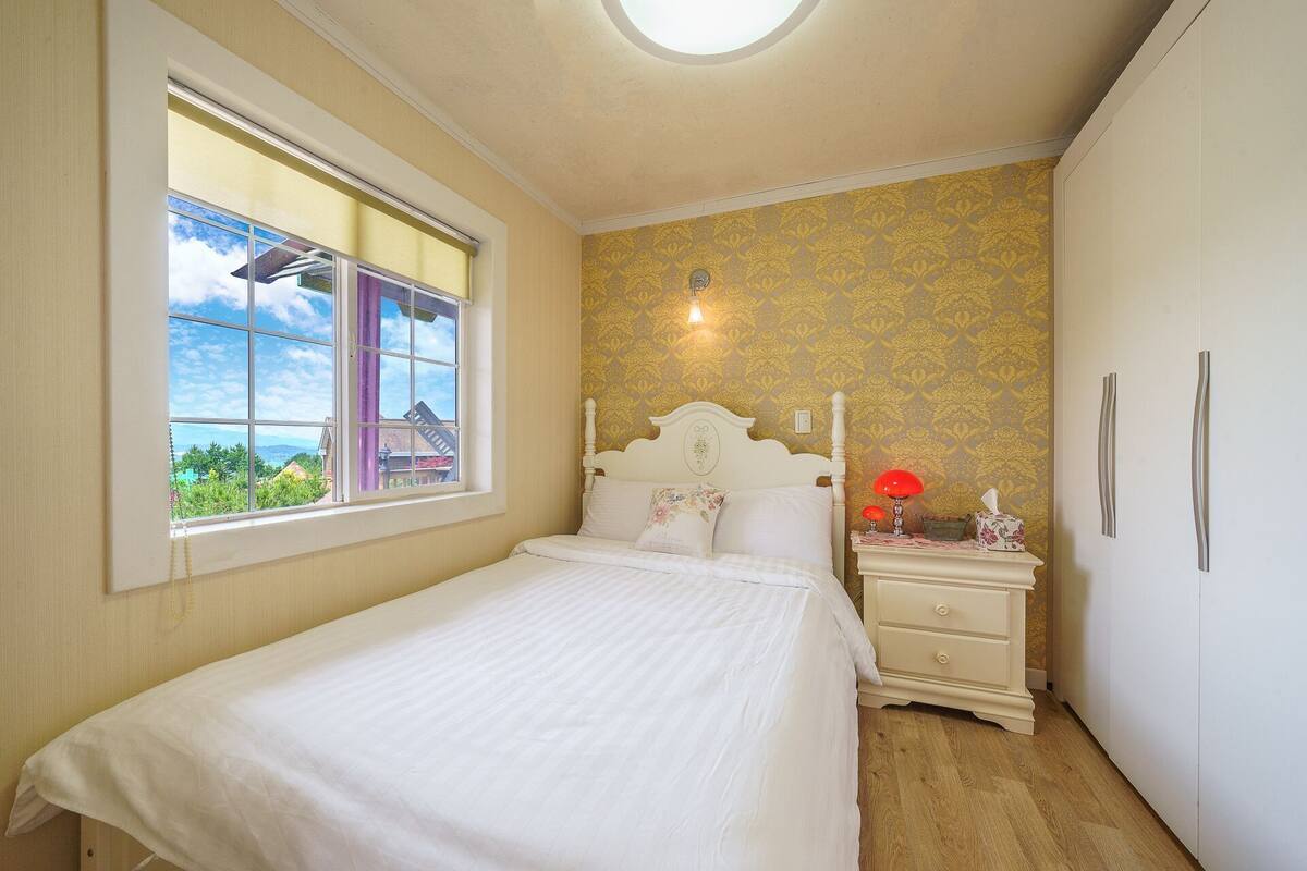 Un dormitorio con cama, mesita de noche, lámpara y ventana con vistas.