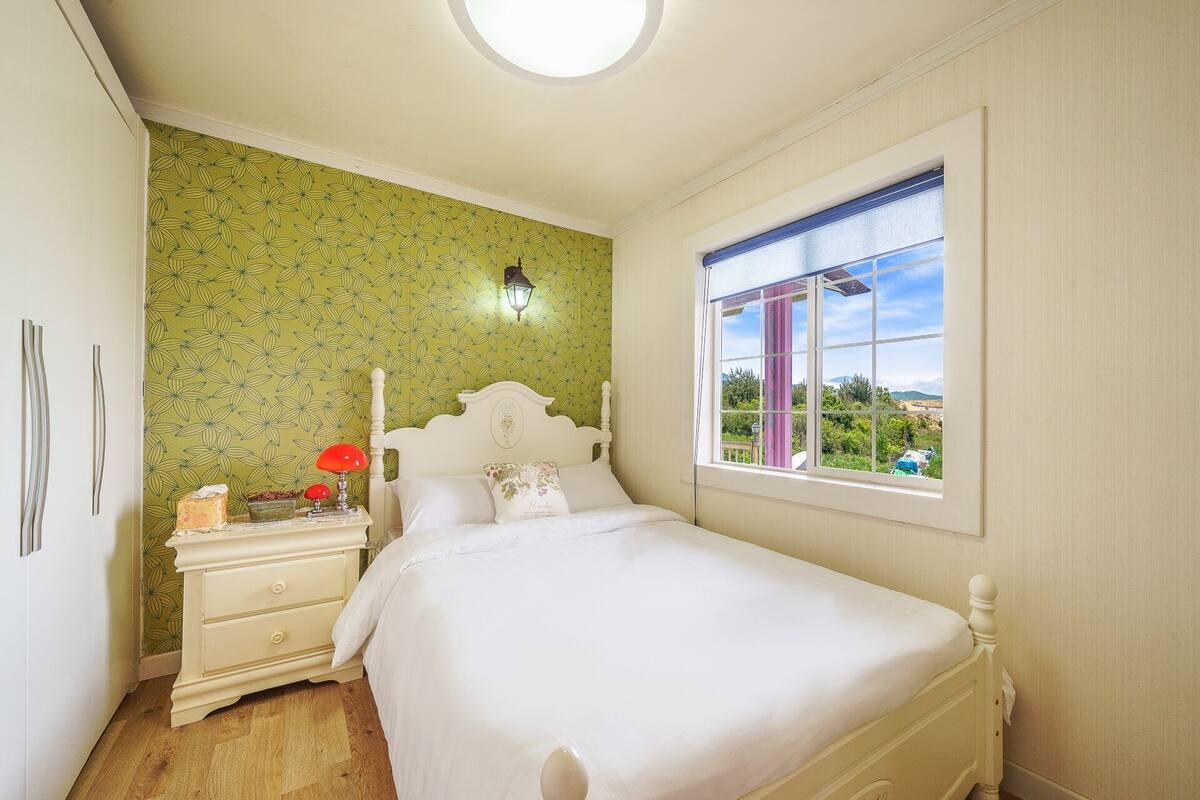 Un dormitorio con cama, mesita de noche, lámpara, ventana y pared con diseño.