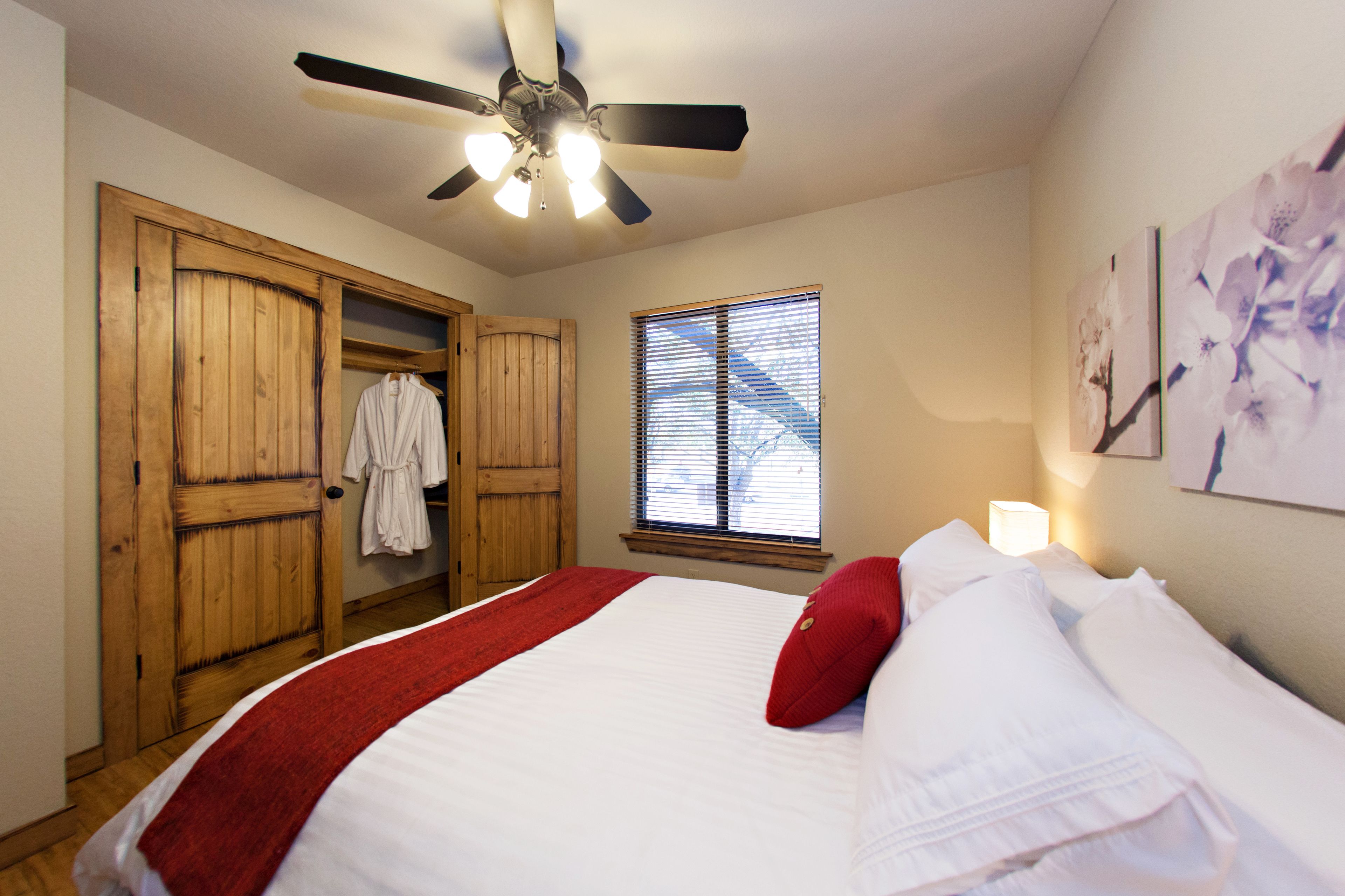 A bedroom with a bed, a ceiling fan, a window with blinds, and a wooden wardrobe.