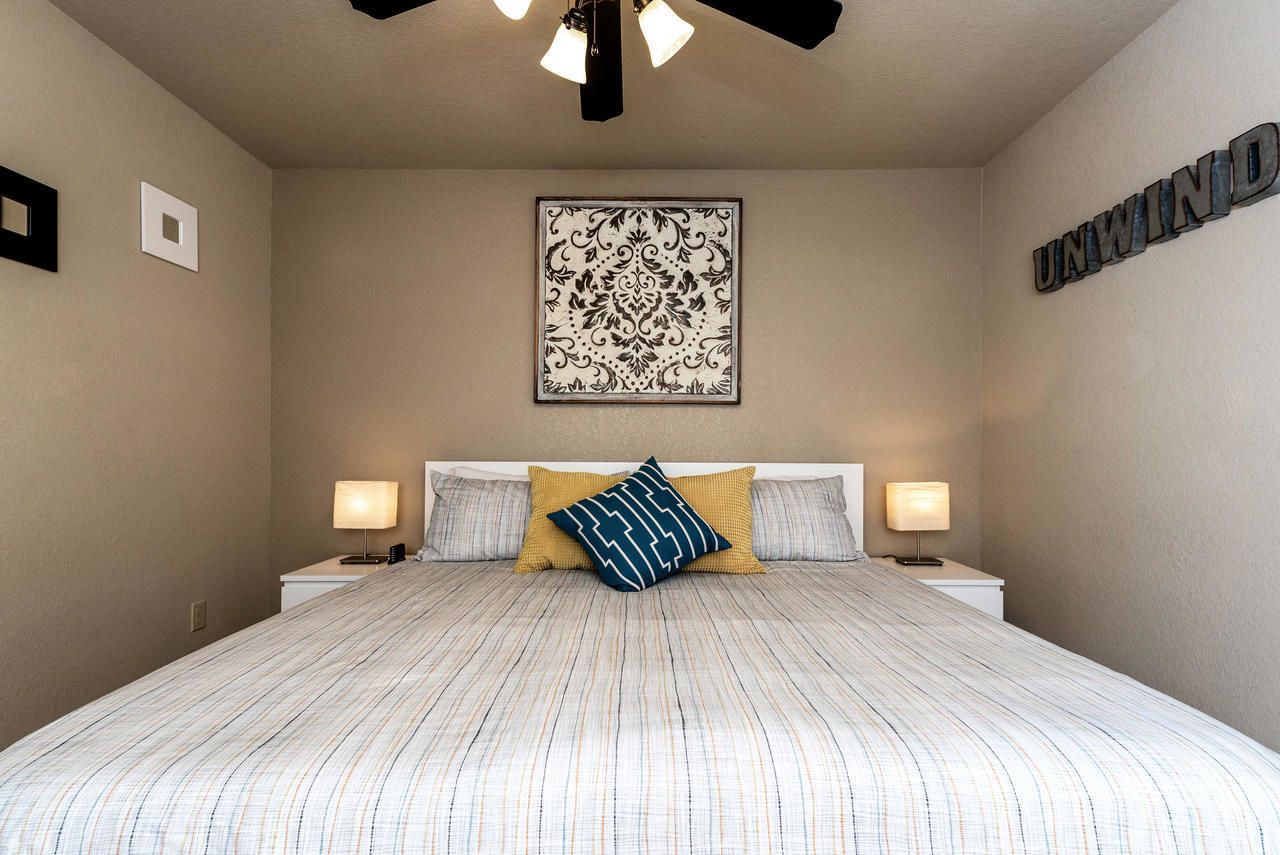 Quarto com cama grande, duas luminárias de cabeceira, um detalhe decorativo na parede e um ventilador de teto.