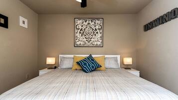 Quarto com cama grande, duas luminárias de cabeceira, um detalhe decorativo na parede e um ventilador de teto.