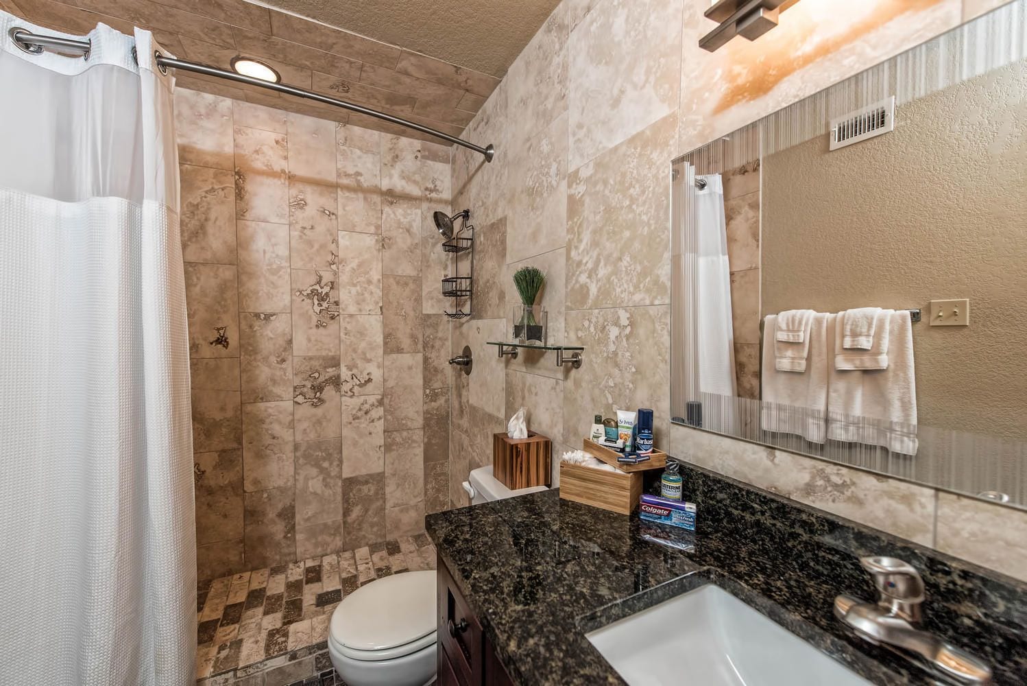 A bathroom with a shower, toilet, sink, and a large mirror.