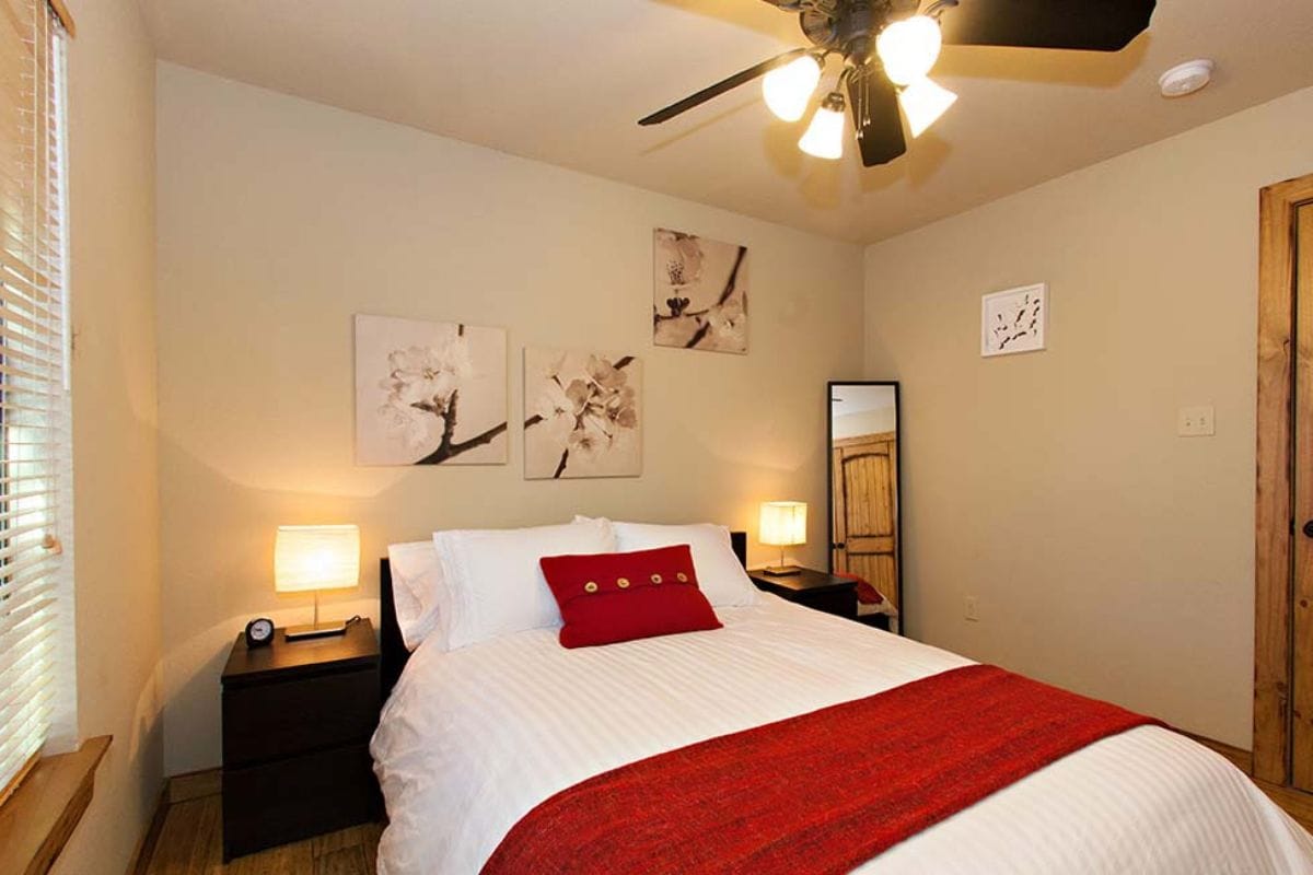 A neatly arranged bedroom with a bed, two bedside tables, a ceiling fan, and wall-mounted artwork.