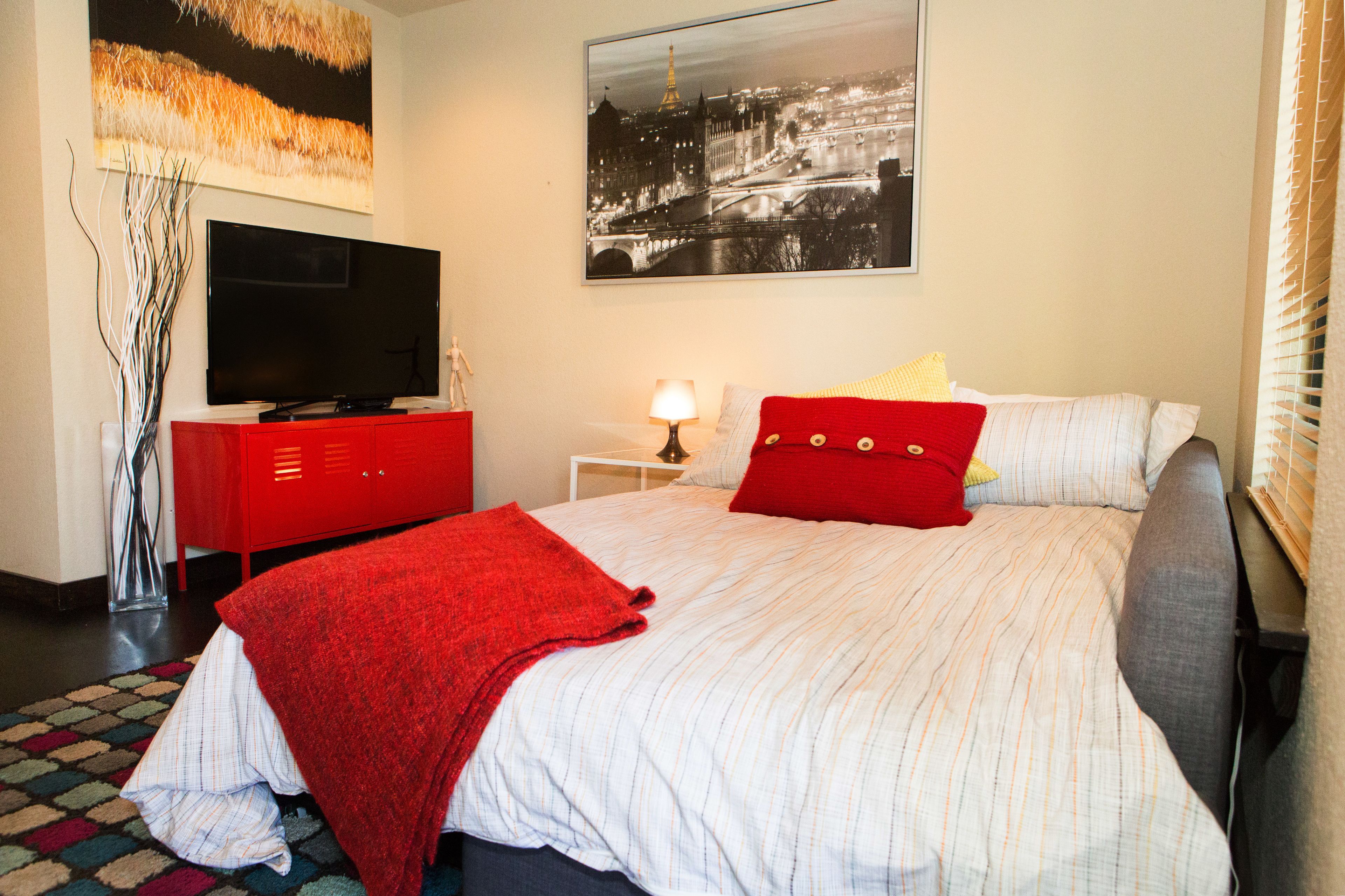 A hotel room with a bed, a TV, a lamp, and a painting on the wall.