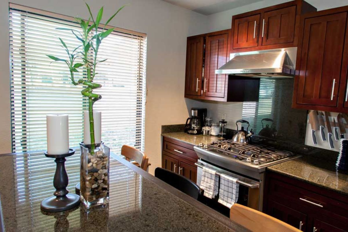 A kitchen with wooden cabinets, a stainless steel stove, and a window with blinds.