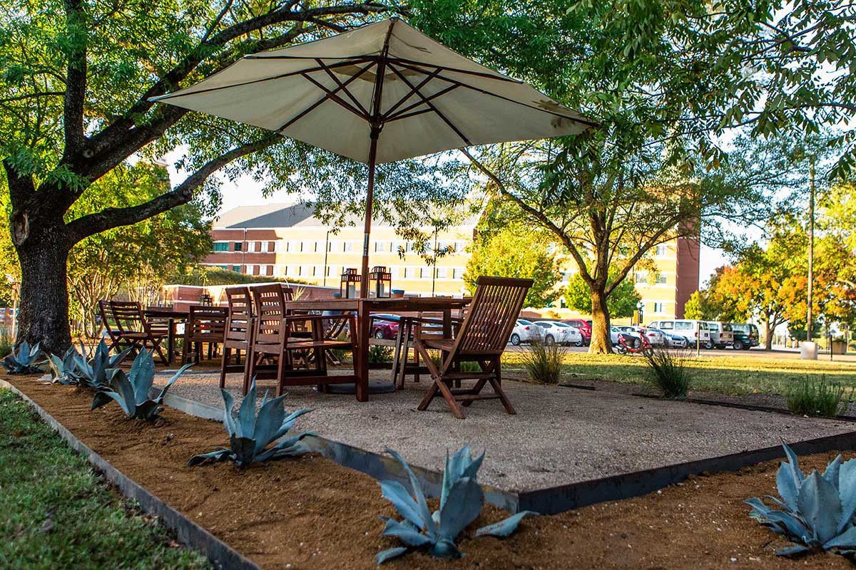 Un patio al aire libre con una mesa y sillas, rodeado de plantas y árboles grandes.