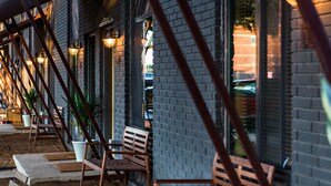 A building with a brick exterior, large windows, and outdoor seating with wooden benches and potted plants. - 1700 South 2nd (Waco)