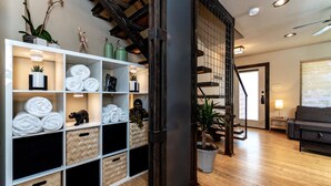 A modern interior with a wooden floor, a white shelving unit with towels, a staircase, and a grey sofa. - 1700 South 2nd (Waco)