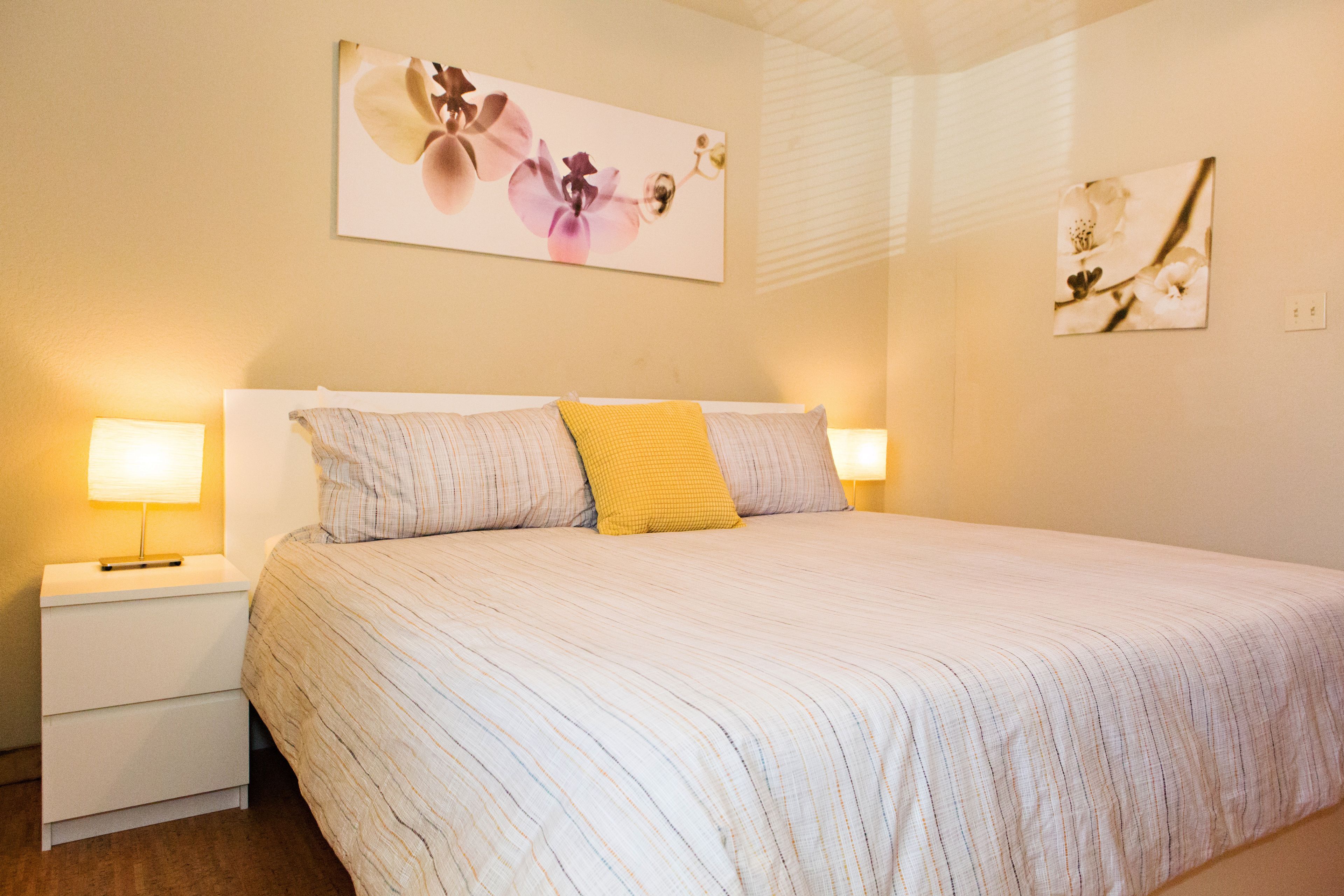 A neatly made bed with striped bedding and a single yellow pillow, flanked by two bedside lamps on white nightstands.