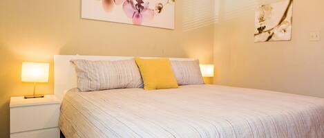 A neatly made bed with striped bedding and a single yellow pillow, flanked by two bedside lamps on white nightstands.
