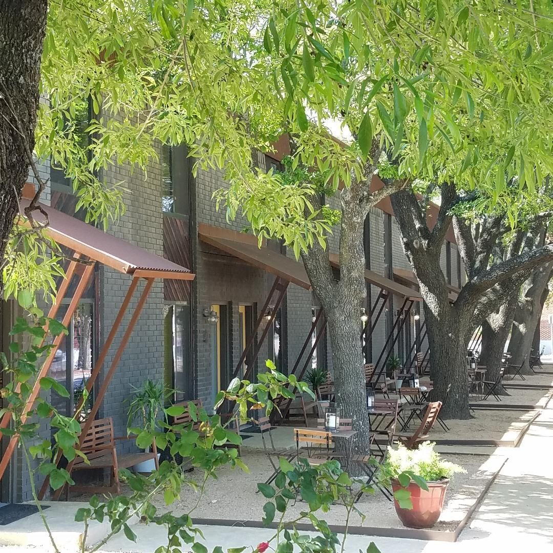 An outdoor seating area with wooden chairs and tables, surrounded by trees and potted plants.