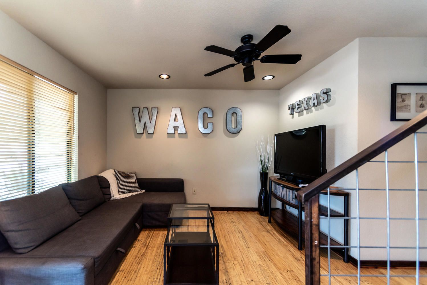 A modern living room with a sofa, a coffee table, a TV, and a ceiling fan.