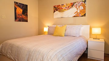 A neatly made bed with striped bedding, two bedside lamps, and two paintings on the walls.