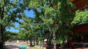 A wooden deck with a pool, surrounded by trees and a building with a green roof. - 1700 South 2nd (Waco)