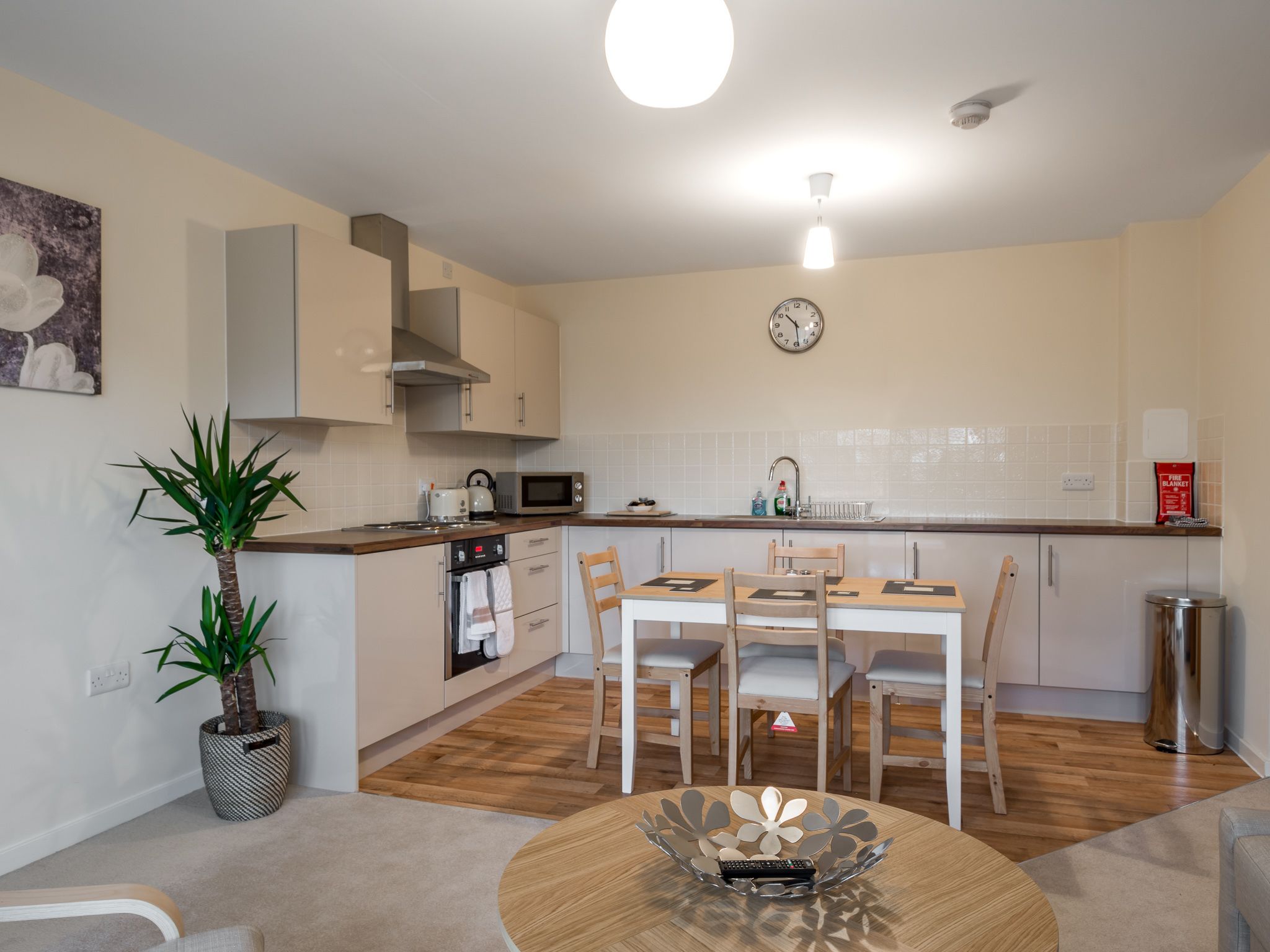 A modern kitchen with a dining area, wooden flooring, and a potted plant.