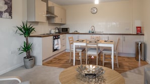 A modern kitchen with a dining area, wooden flooring, and a potted plant. - Luxury 2 Bed Riverside (Bedford)