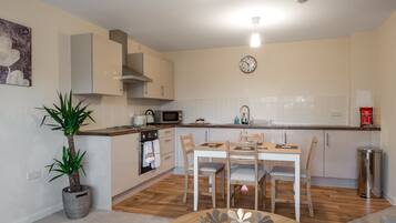 A modern kitchen with a dining area, wooden flooring, and a potted plant.