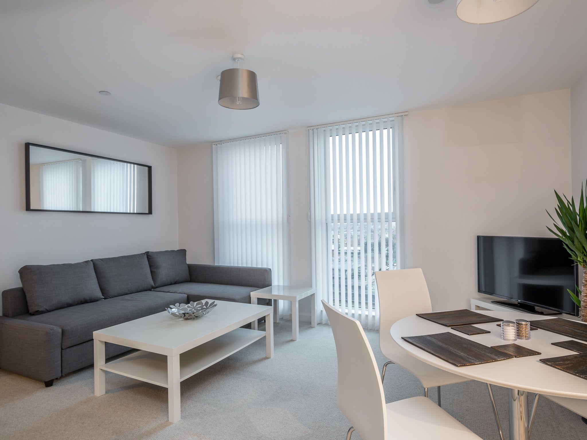 A modern living room with a grey sofa, white coffee table, and a dining area with a round table and chairs.