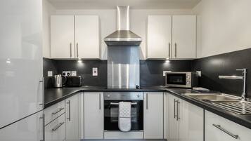 A modern kitchen with white cabinets, a stainless steel range hood, a built-in oven, a microwave, and a black countertop.