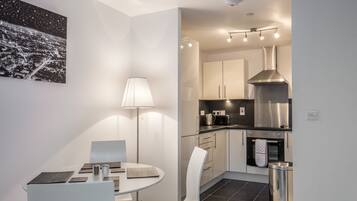 A modern kitchen with white cabinets, a stainless steel range hood, and a black countertop. There is a dining area with a round table and white chairs.