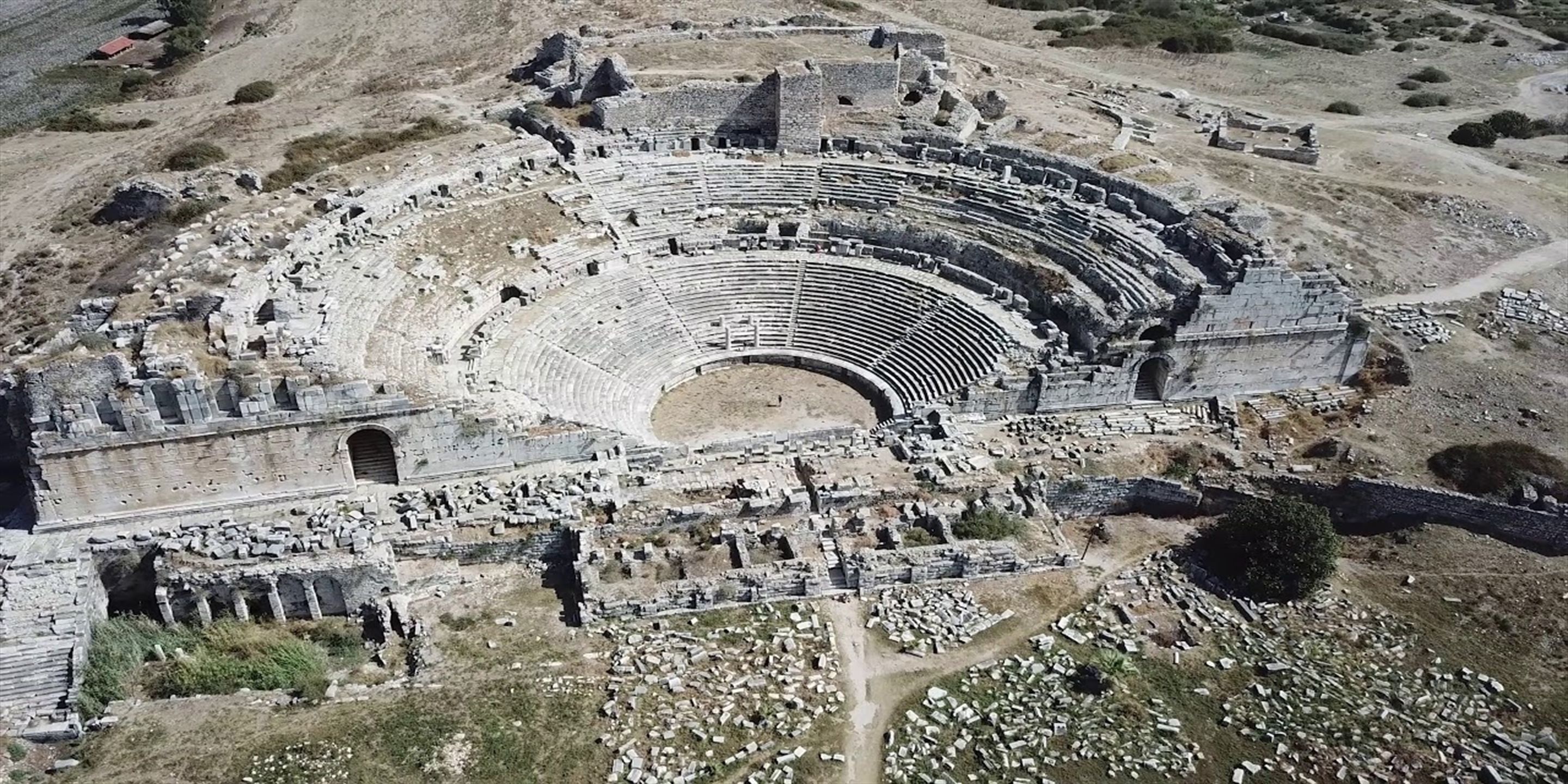 An ancient amphitheater with tiered seating and ruins scattered around.