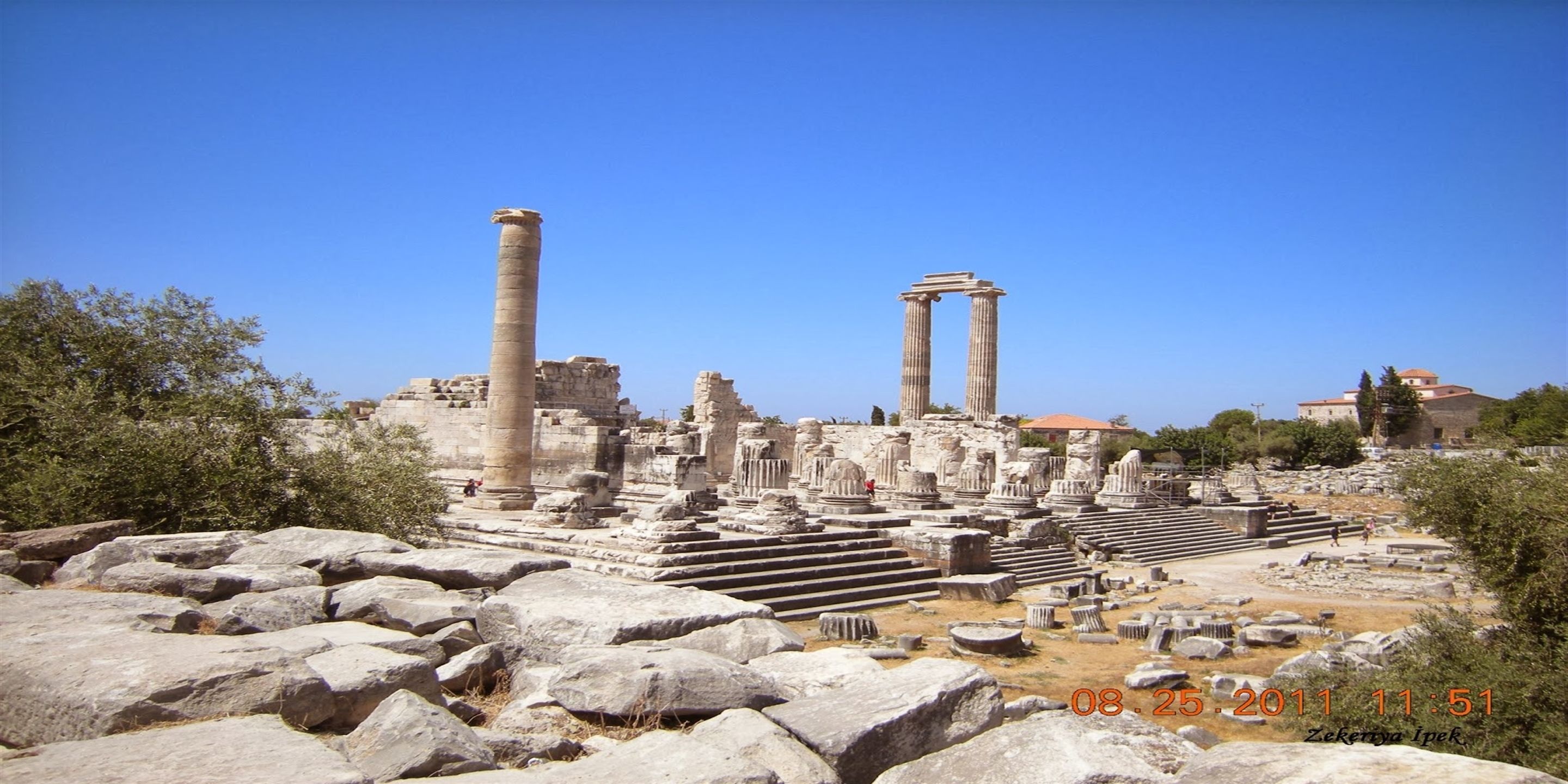 Ruinas antiguas con columnas y escalones, rodeadas de grandes rocas y árboles.