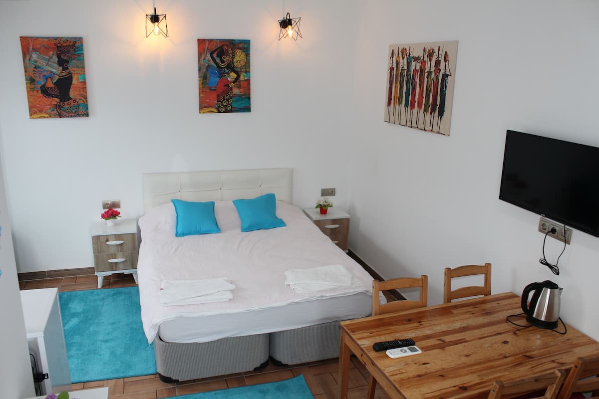 A hotel room with a bed, a TV, a wooden table, and artwork on the walls.