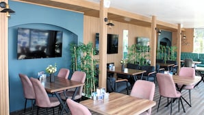 Un restaurante moderno con mesas y sillas de madera, una pantalla de televisión grande y plantas de interior.
