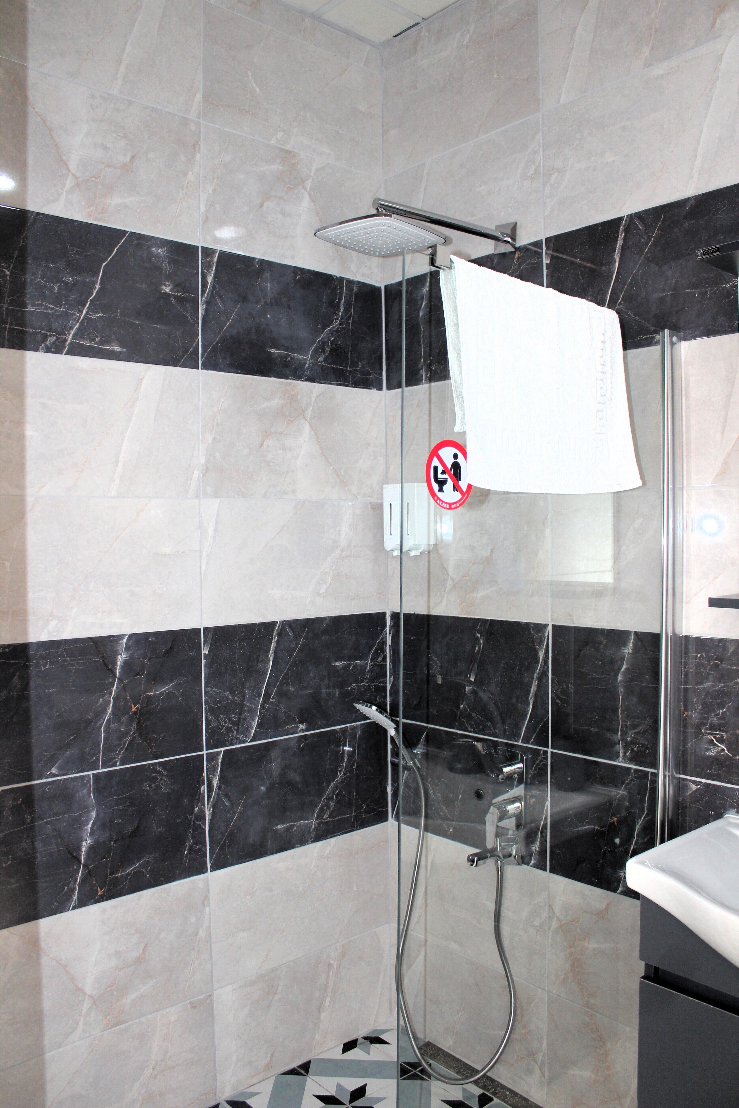 Un baño moderno con baldosas de mármol blanco y negro, cerramiento de ducha de vidrio y lavamanos blanco.