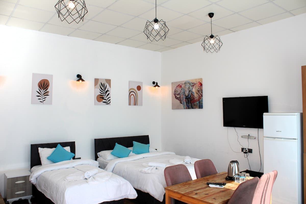 A hotel room with two beds, a dining table, a television, and artwork on the walls.