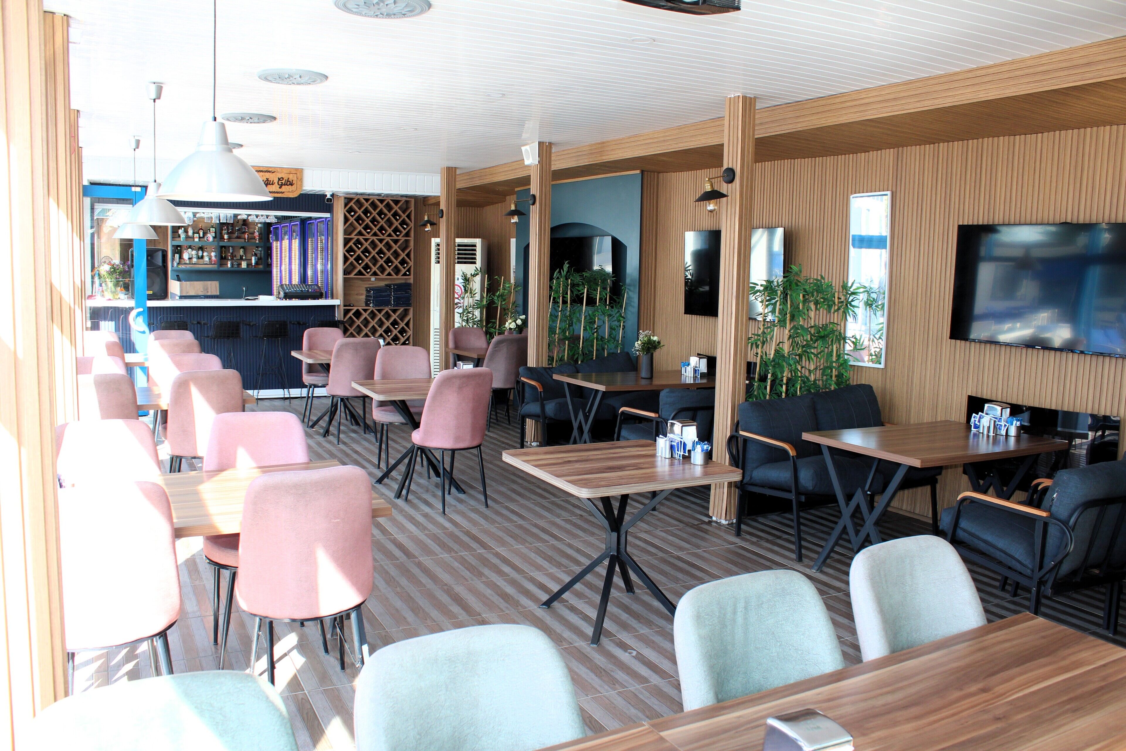Un restaurante moderno con varias zonas de estar, incluyendo mesas y sillas, y una zona de bar con estanterías llenas de botellas.