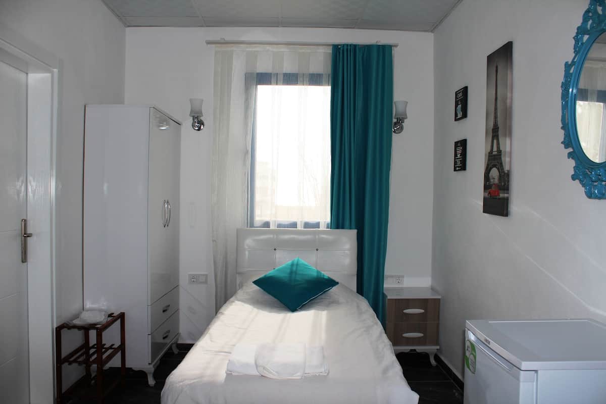 A small, clean room with a bed, a wardrobe, a desk, and a window with curtains.