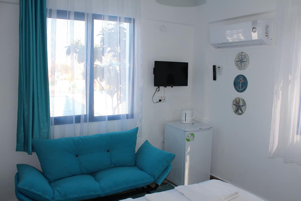 A room with a teal sofa, a small white cabinet, a flat-screen TV, and decorative plates on the wall.