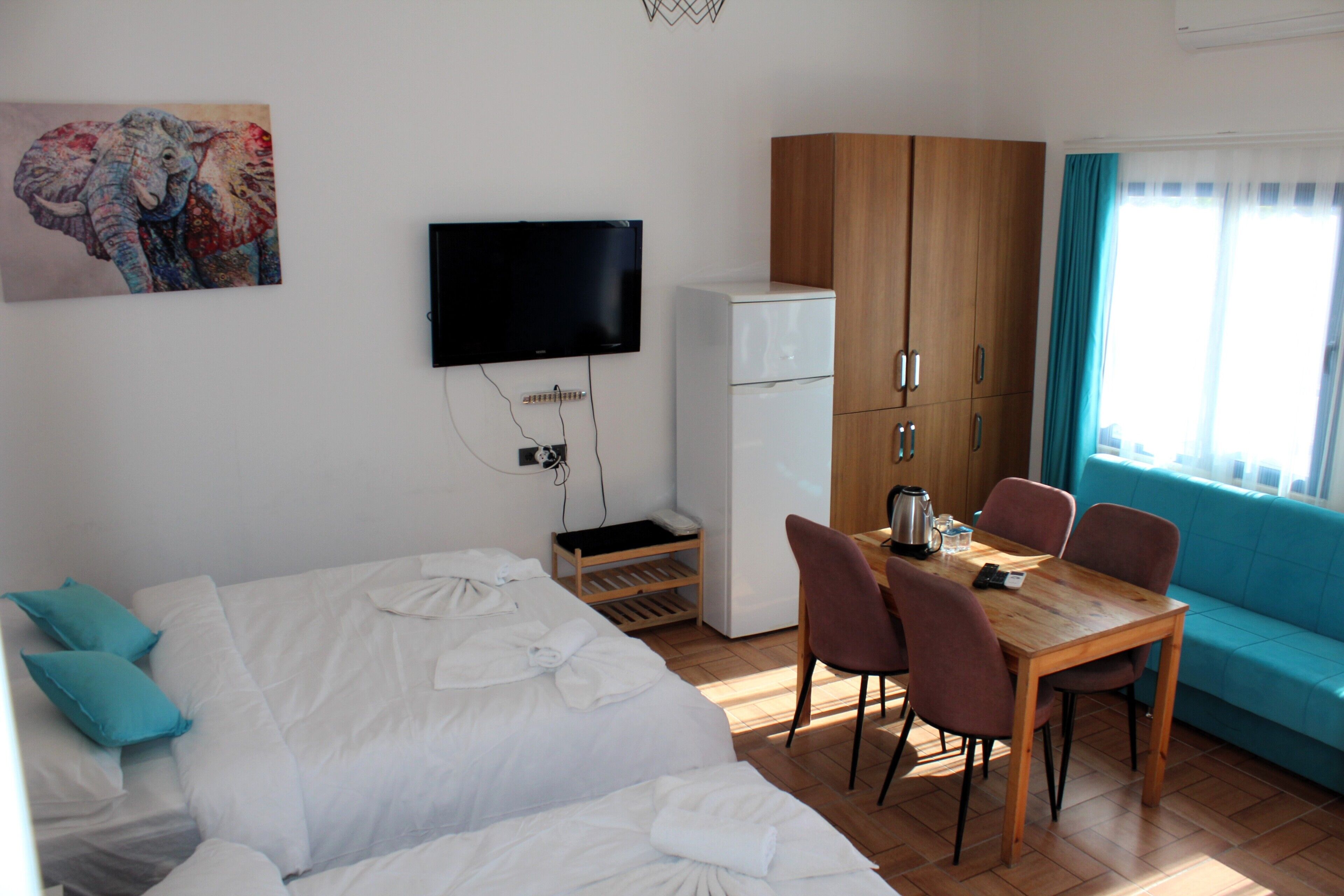 A hotel room with a bed, a desk with chairs, a television, a refrigerator, and a sofa.