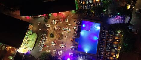 An aerial view of a hotel courtyard with multiple dining areas, outdoor seating, and a pool.