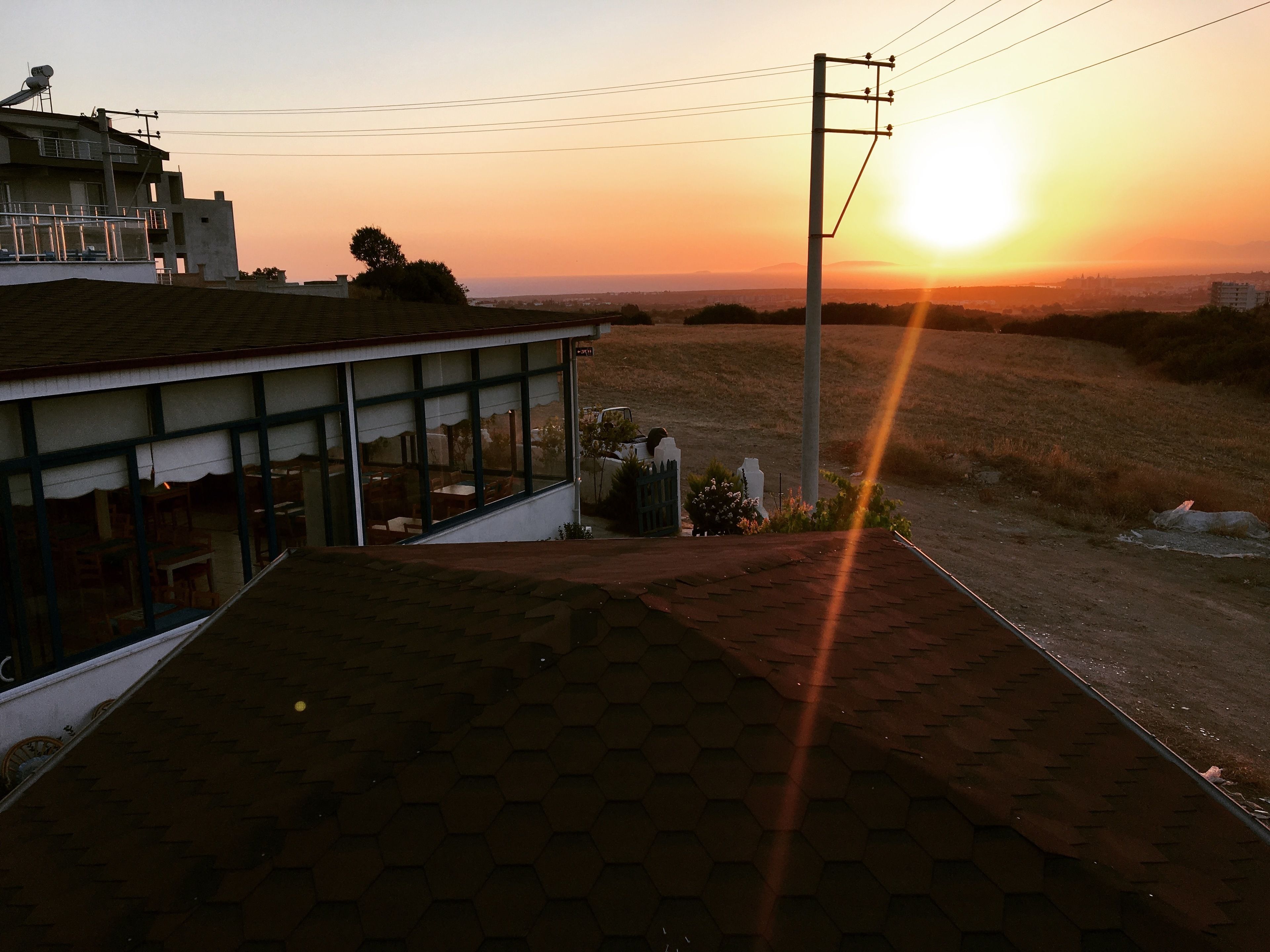 Un edificio con tejado de baldosas hexagonales, un espacio al aire libre con mesas y sillas, y vista del atardecer sobre un paisaje montañoso.
