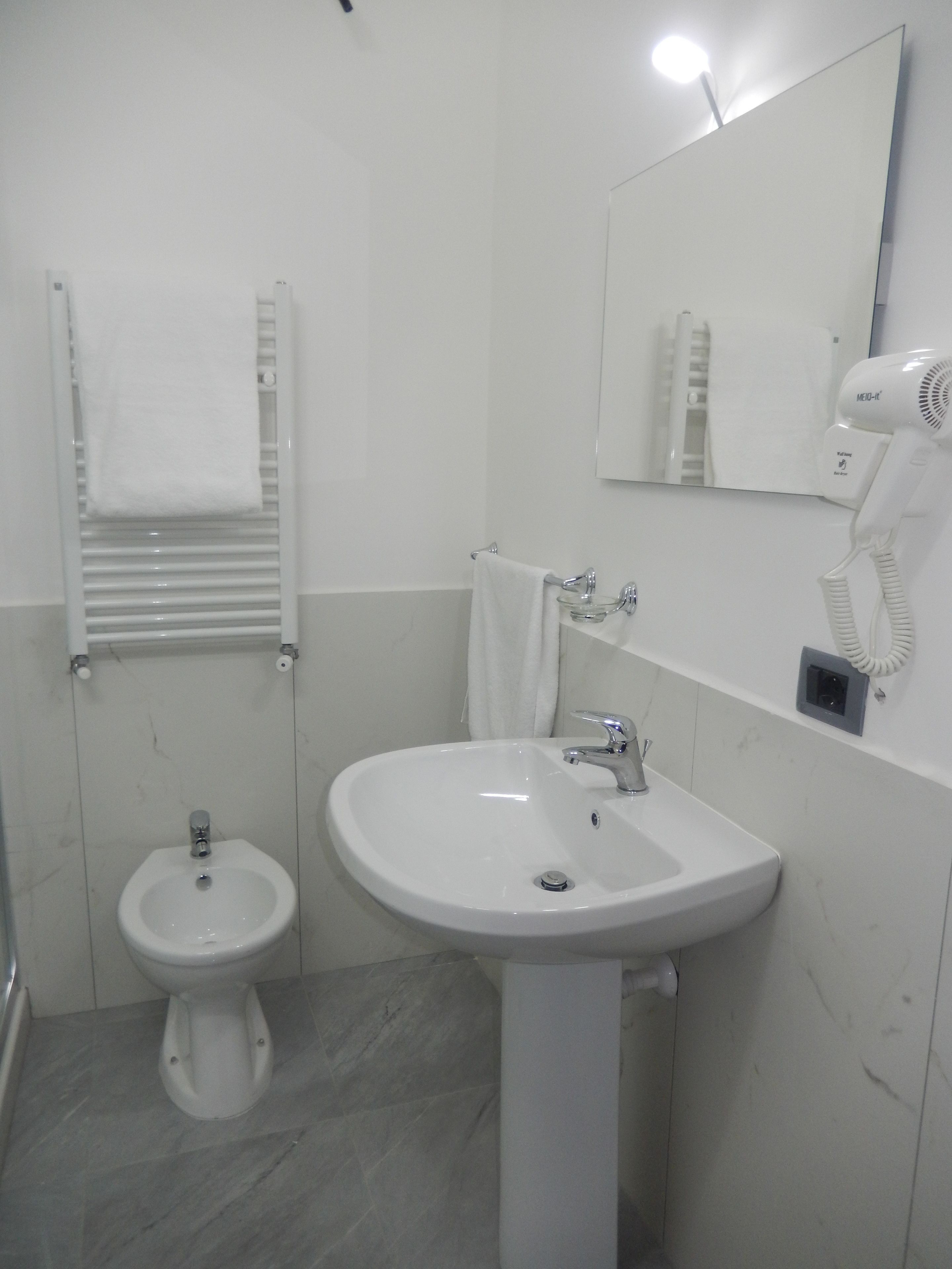 Uma casa de banho com lavatório assentado, um bidé, um porta-toalhas, um espelho e um secador de cabelo.