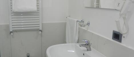 Uma casa de banho com lavatório assentado, um bidé, um porta-toalhas, um espelho e um secador de cabelo.