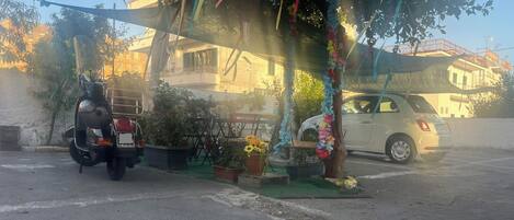 A parking area with a scooter, a car, and potted plants.