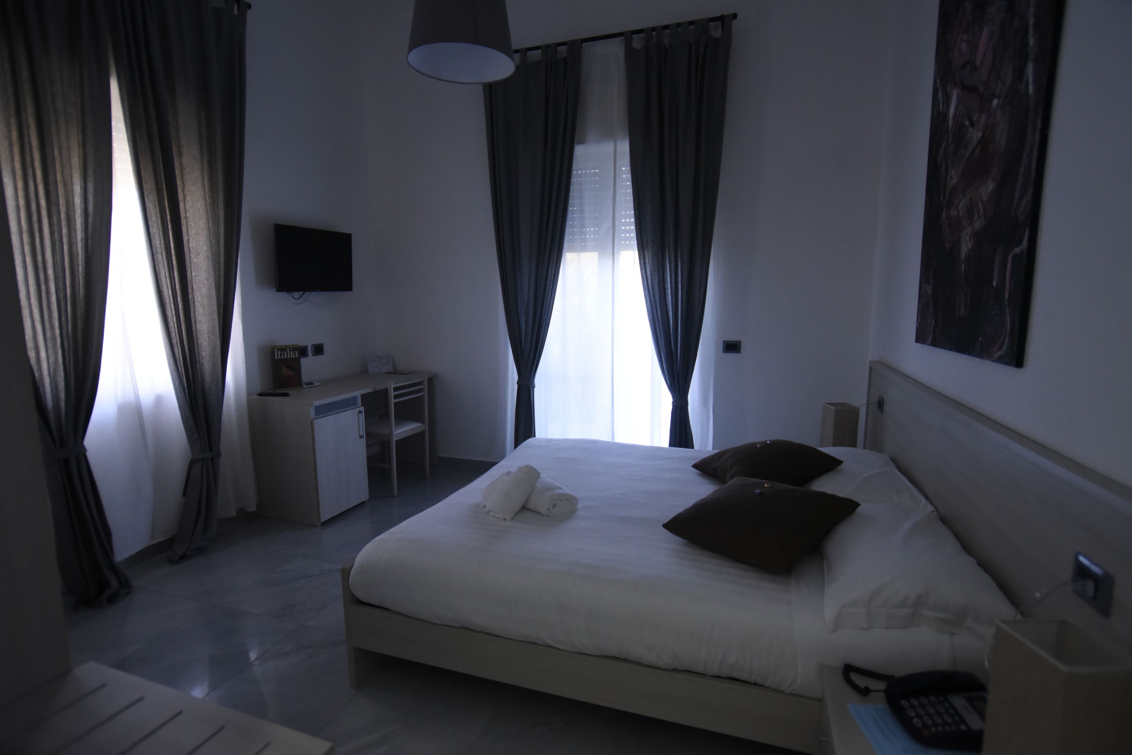 A hotel room with a bed, a desk, a chair, a TV, and a window with curtains.