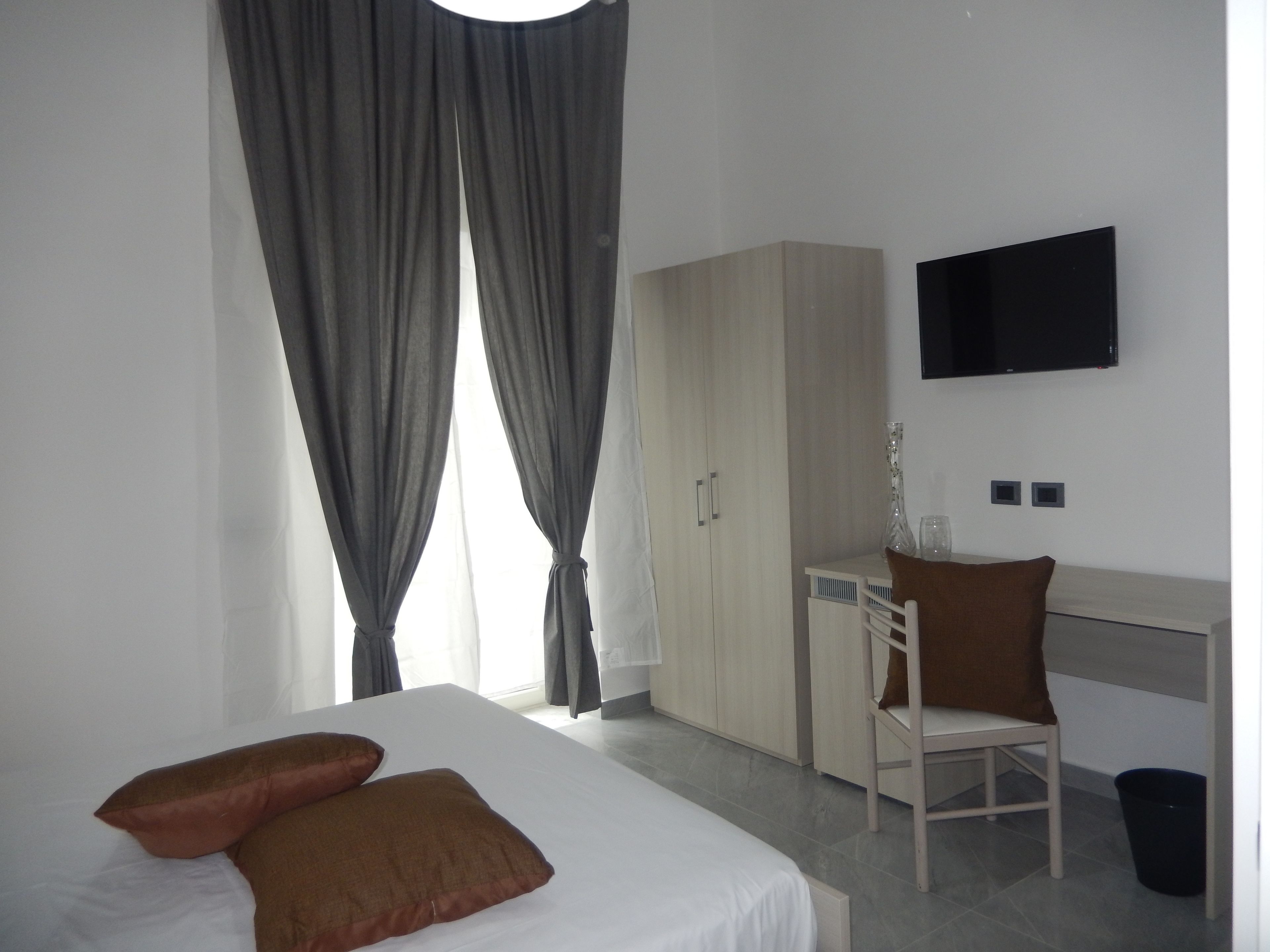 A hotel room with a bed, a desk, a chair, and a TV mounted on the wall.