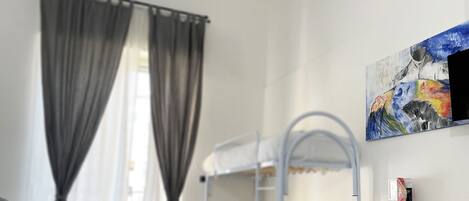 Una habitación de hotel con literas, un cuadro en la pared, una ventana con cortinas y un folleto sobre la cama.