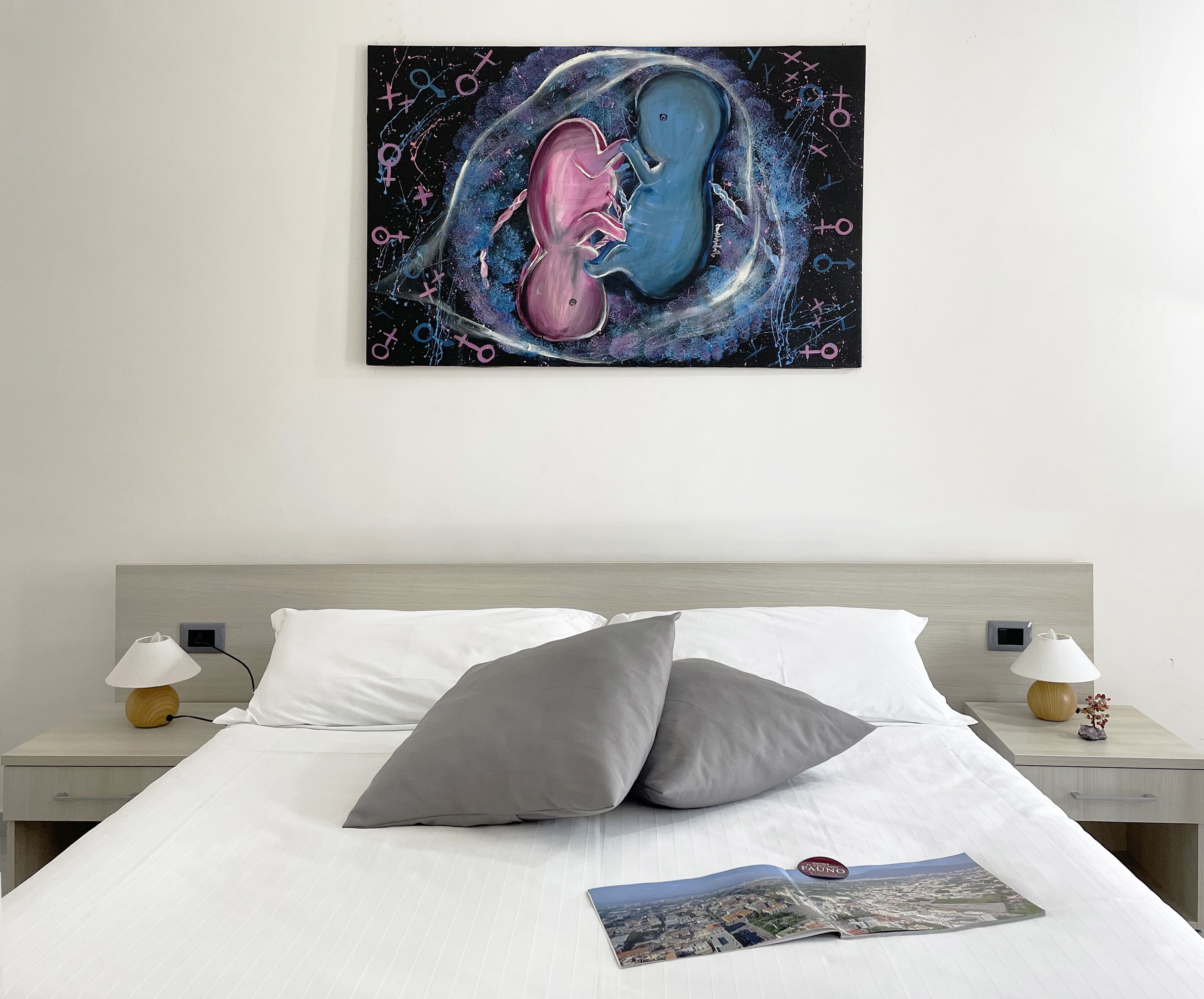 Habitació d'hotel amb un llit, dues taules de nit, una estantalla i una revista sobre el llit.